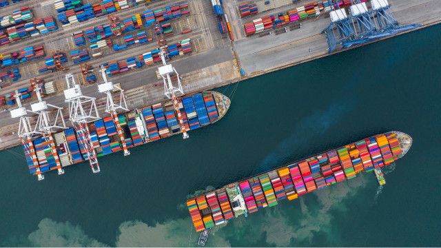 An aerial view of a cargo ship terminal with unloading cranes, containers, and container ships